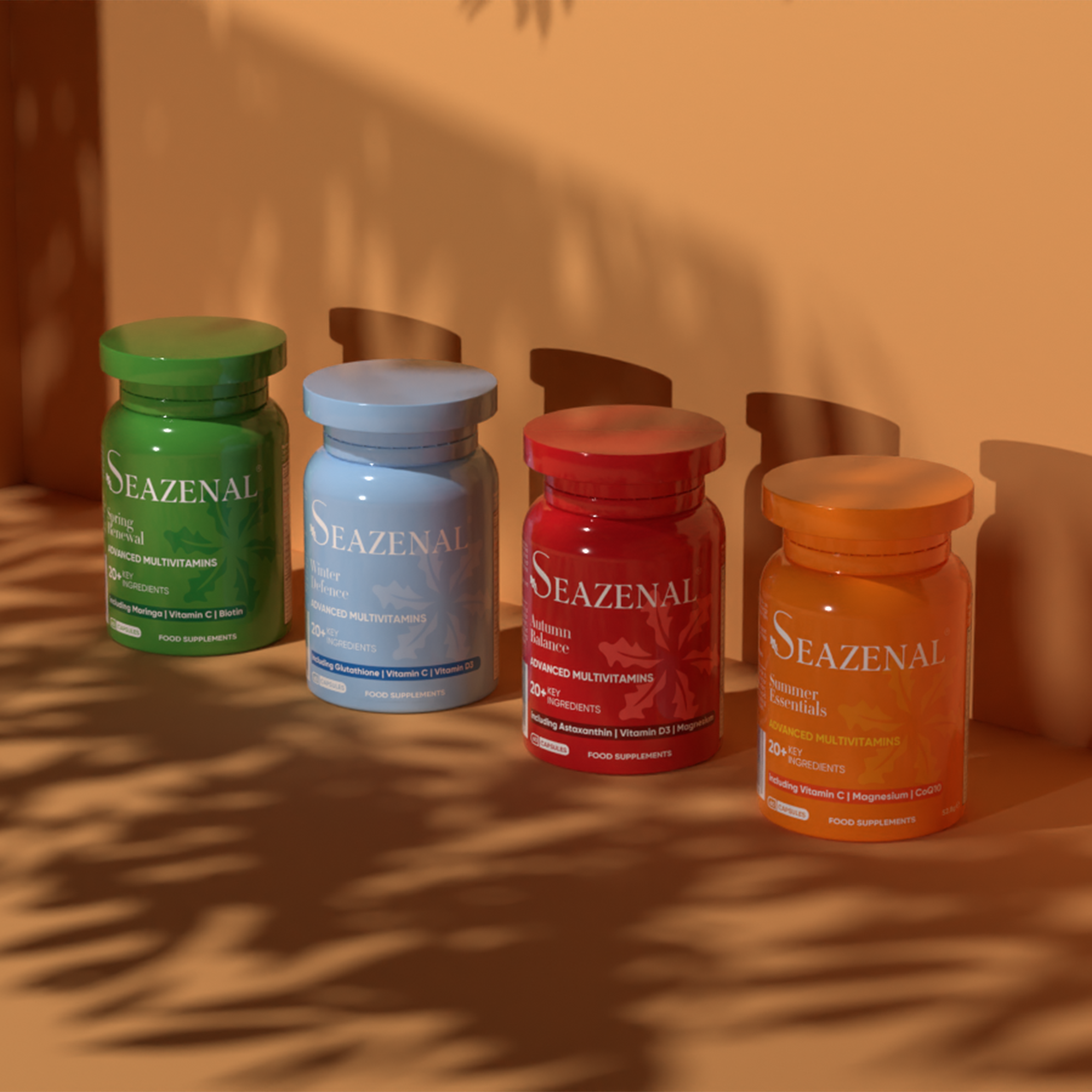 Four Seazenal multivitamin supplement capsules bottles in green, blue, red, and orange on a orange surface with a warm brown background and shadows of leaves. premium bottles
